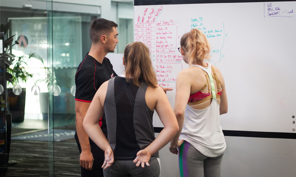 Athletes being shown their programme on a whiteboard by their coach